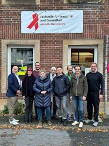 Gruppe von Personen vor einem Gebäude, an dem ein Banner der Aidshilfe in Münster hängt.