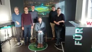 Gruppe von fünf Personen vor einem Bild des Stadions