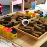 Buchstaben aus Holz und Spielsachen auf einem kleinen Tisch, im Hintergrund ein Kinderstuhl und ein Kinderpiano