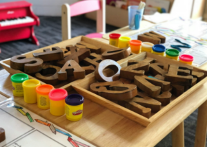 Buchstaben aus Holz und Spielsachen auf einem kleinen Tisch, im Hintergrund ein Kinderstuhl und ein Kinderpiano